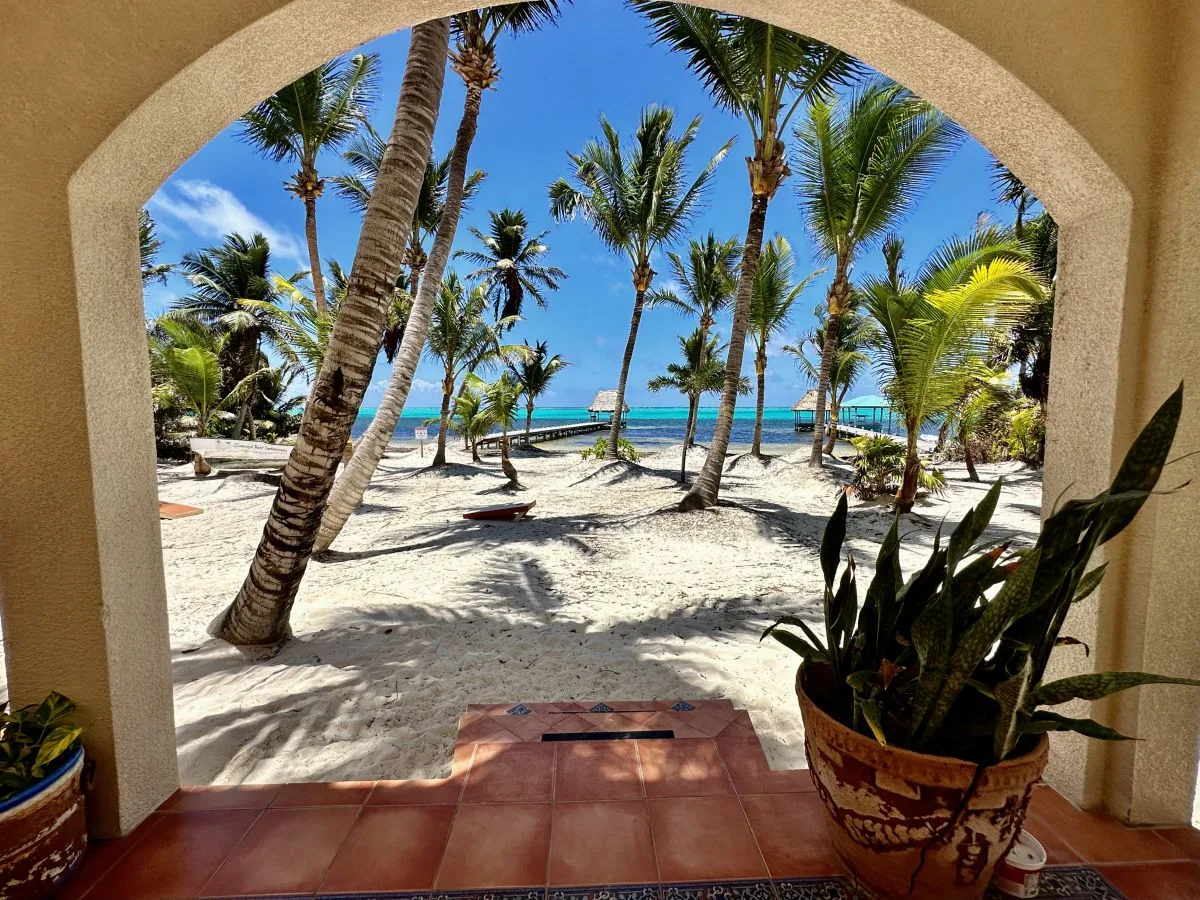 A sandy palm-lined beach and turquoise water are framed by a tiled archway.