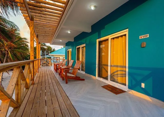 A covered outdoor balcony with wooden seating beside teal walls and glass doors.