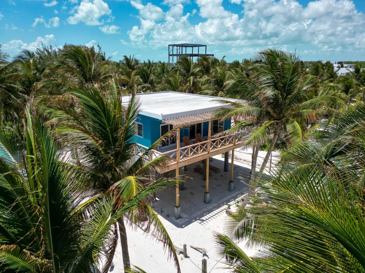 A raised building with a wooden balcony stands among palm trees.