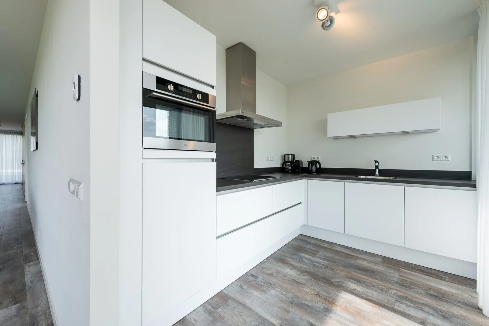 A modern white kitchen with built-in appliances, dark countertops, and wood-look flooring.