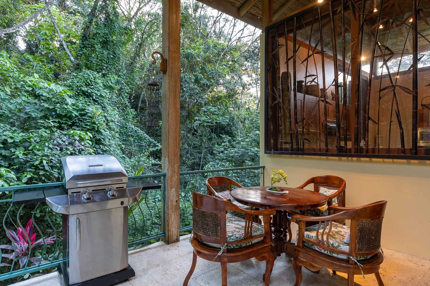 Una terraza cubierta con mesa de comedor y parrilla da a una densa vegetación.