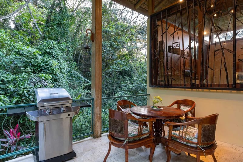Villa Michelina · 28. A Balinese-inspired outdoor terrace with a tiled floor and bamboo roof features a dining table and grill, offering views directly into the dense tropical jungle canopy.