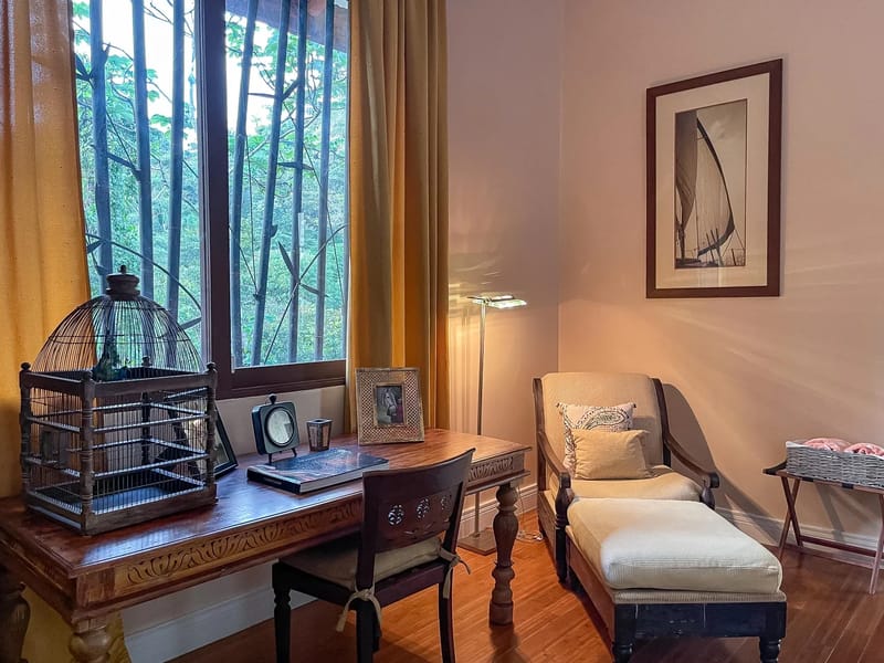 Villa Michelina · 13. This private space provides a comfortable wooden desk and chaise lounge, illuminated by natural light from a large window overlooking a lush tropical landscape.