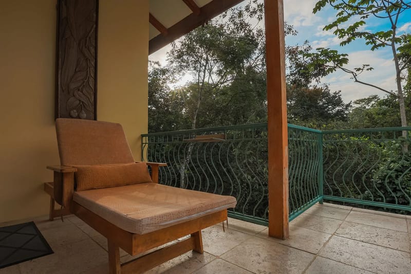 Villa Michelina · 15. A private covered balcony, featuring a carved wall panel and a comfortable chaise lounge, opens to immersive views of the dense tropical canopy.