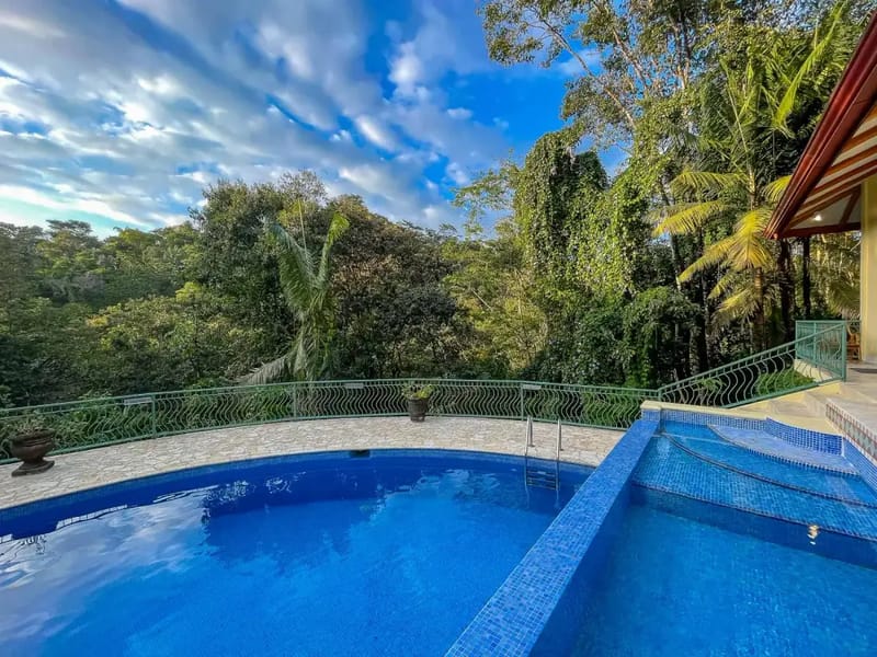 Villa Michelina · 22. An outdoor tiled main pool and a connected wade pool are set on a terrace with a railing, offering views of the dense tropical canopy against a blue sky.
