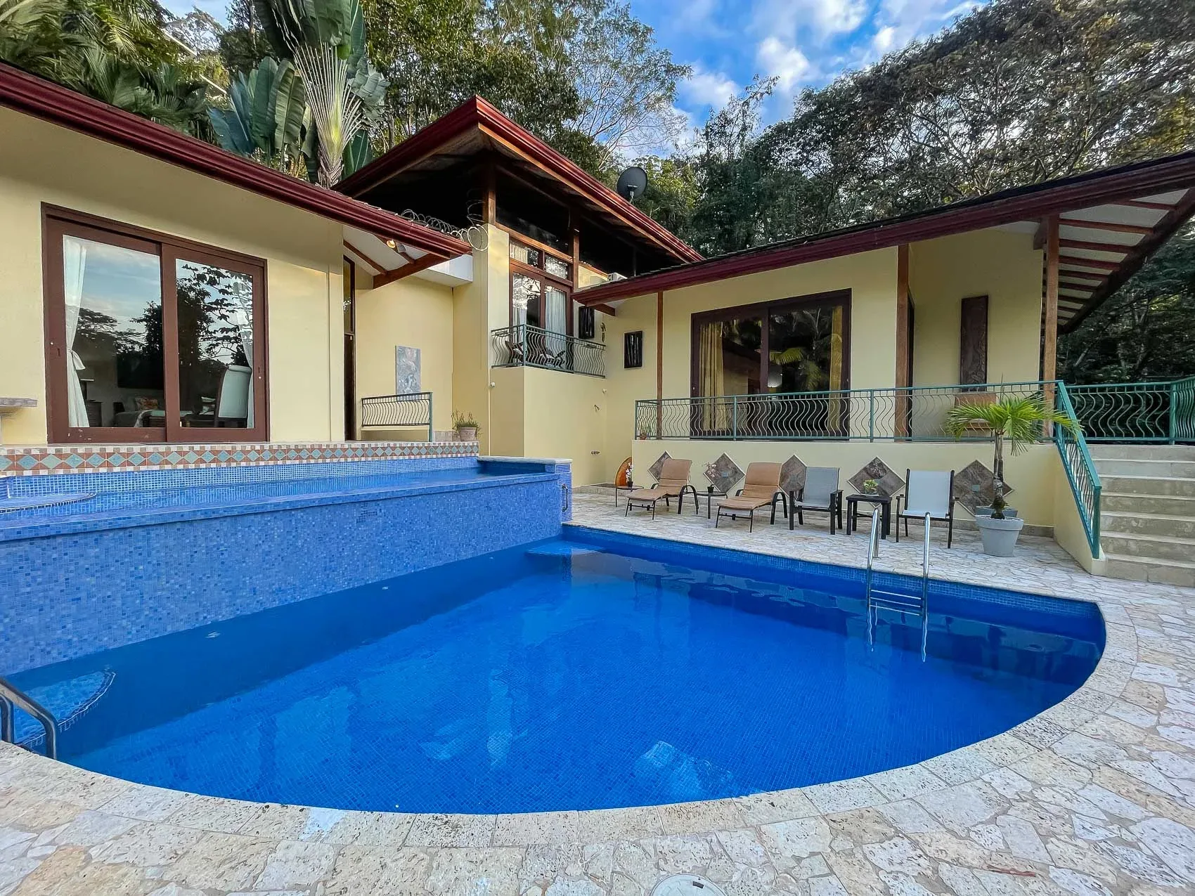 Una piscina azul ocupa el primer plano, con asientos al aire libre junto a la villa.