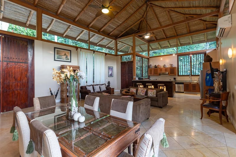 Villa Michelina · 7. This open-plan living, dining, and kitchen space combines a high vaulted bamboo ceiling with exposed wooden beams, ample natural light, and immersive views into dense tropical foliage.