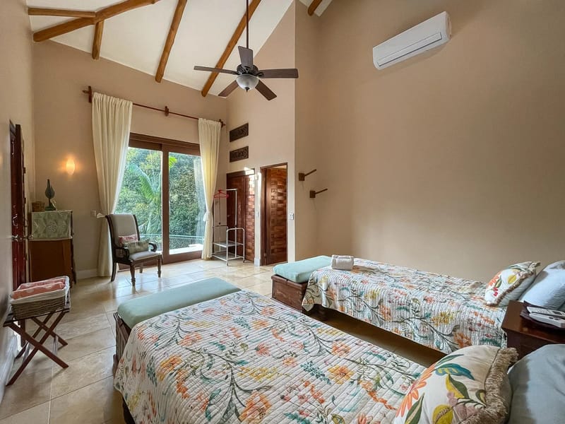 Villa Michelina · 19. This spacious bedroom features two individual beds, a vaulted ceiling with exposed wooden beams, and glass sliding doors that open to a lush jungle view, creating an open and bright atmosphere.