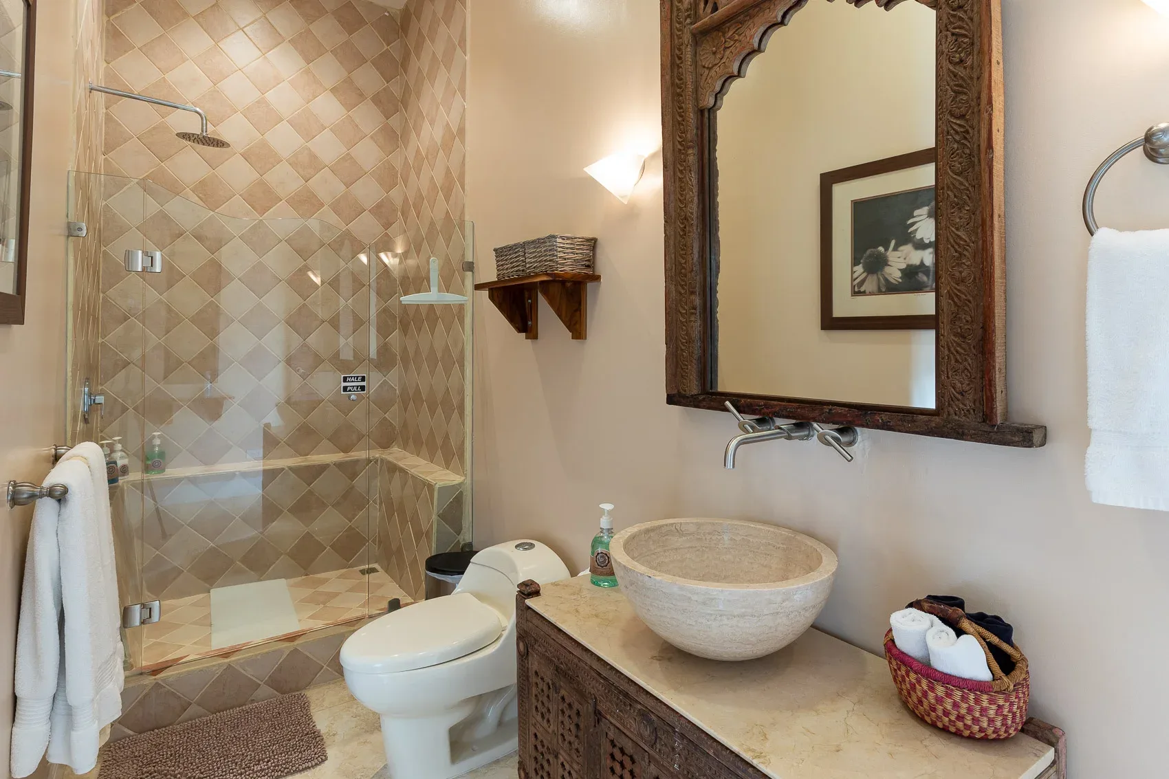 Baño con ducha revestida de azulejos, inodoro y lavabo tipo cuenco bajo un espejo enmarcado.