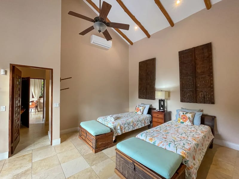 Villa Michelina · 18. This bedroom offers a high vaulted ceiling with exposed wooden beams, contains two individual beds, and is styled with Balinese-inspired wooden details.
