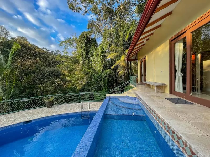 Villa Michelina · 27. A main pool and an integrated wade pool are positioned on a tiled patio, offering direct views of lush tropical jungle under a clear sky, with glass doors opening into the villa.