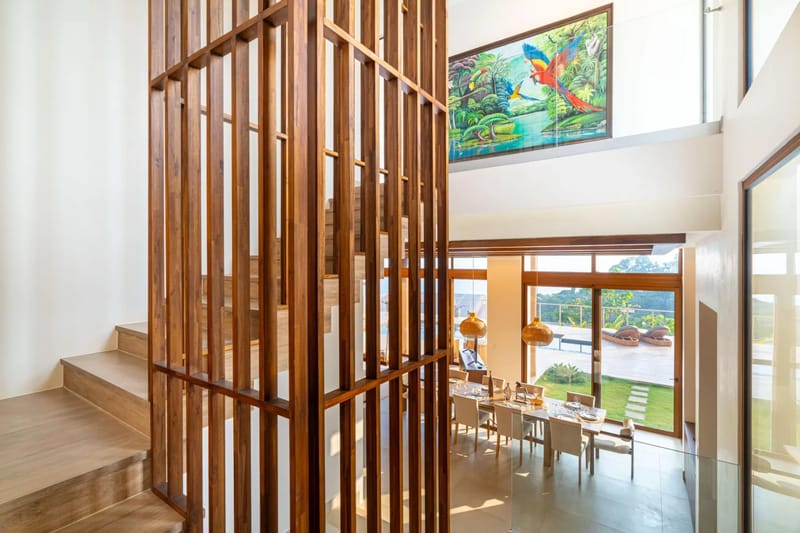 Casa Bella Vina · 9. Este espacio luminoso de planta abierta cuenta con una destacada escalera de listones de madera, un comedor con una larga mesa de madera y amplias puertas de vidrio que dan a una terraza con vistas a la selva y al océano.