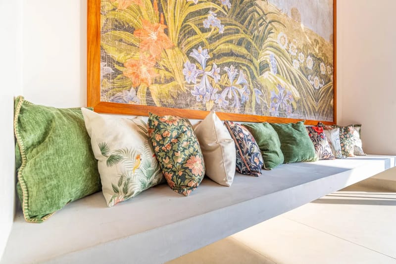 Casa Bella Vina · 17. Un banco integrado de concreto con varios cojines estampados se encuentra debajo de una gran obra de arte tropical enmarcada, bañado por la luz natural.