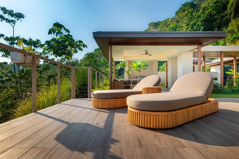 Casa Bella Vina · 19. Una terraza de madera iluminada por el sol cuenta con tumbonas y una sala de estar exterior cubierta, y se abre a vistas de una exuberante selva tropical y un cielo azul despejado.