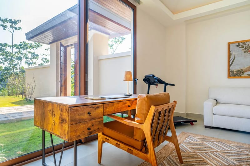 Casa Bella Vina · 13. La suite de invitados cuenta con un escritorio y una silla de madera, un sofá y una caminadora, con abundante luz natural que entra por grandes ventanas con vistas al jardín tropical.