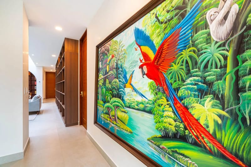 Casa Bella Vina · 15. Un luminoso pasillo con biblioteca cuenta con amplias estanterías de madera oscura, iluminación empotrada y un gran mural colorido que representa una vibrante escena de selva tropical.