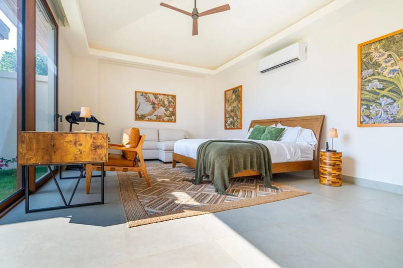 Casa Bella Vina · 11. Un luminoso dormitorio de invitados cuenta con una cama king, un sofá y un escritorio de trabajo, con grandes puertas de vidrio que proporcionan abundante luz natural y vistas al paisaje tropical circundante.