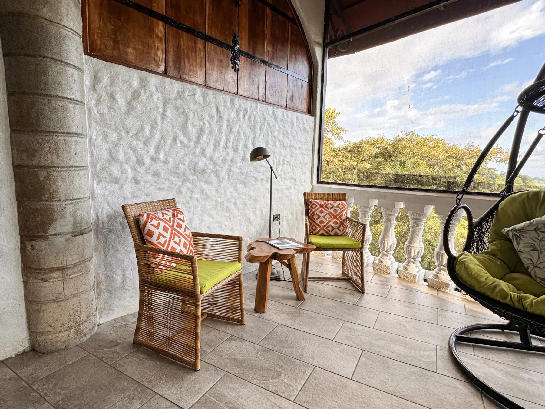 A covered balcony seating area with woven chairs and a view of trees.