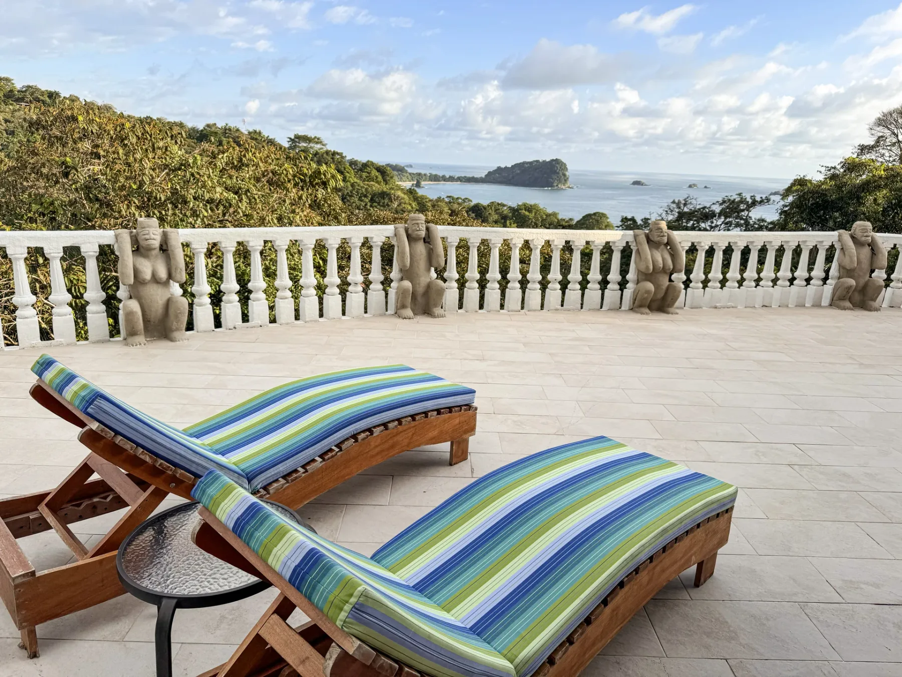 An outdoor terrace has striped lounge seating overlooking the sea.