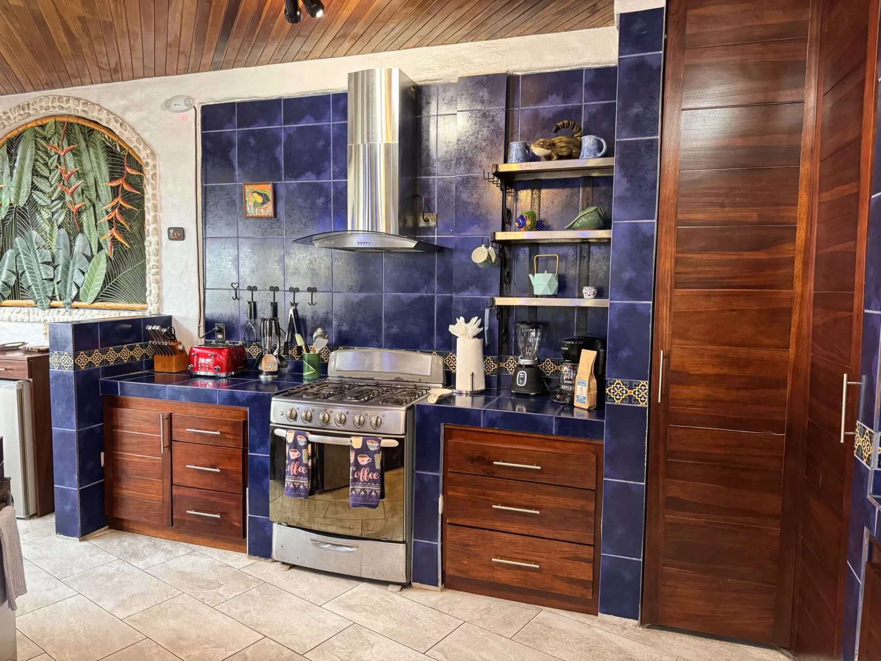 A tiled kitchen with wooden cabinets, a stove, and open shelves.
