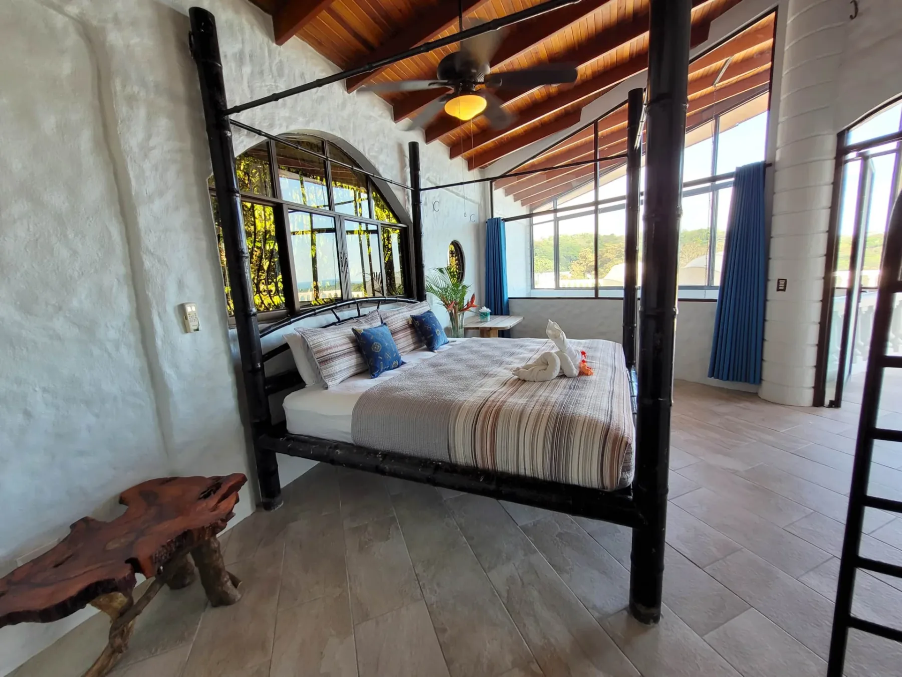 A bedroom with a four-poster bed beneath a sloped wooden ceiling.