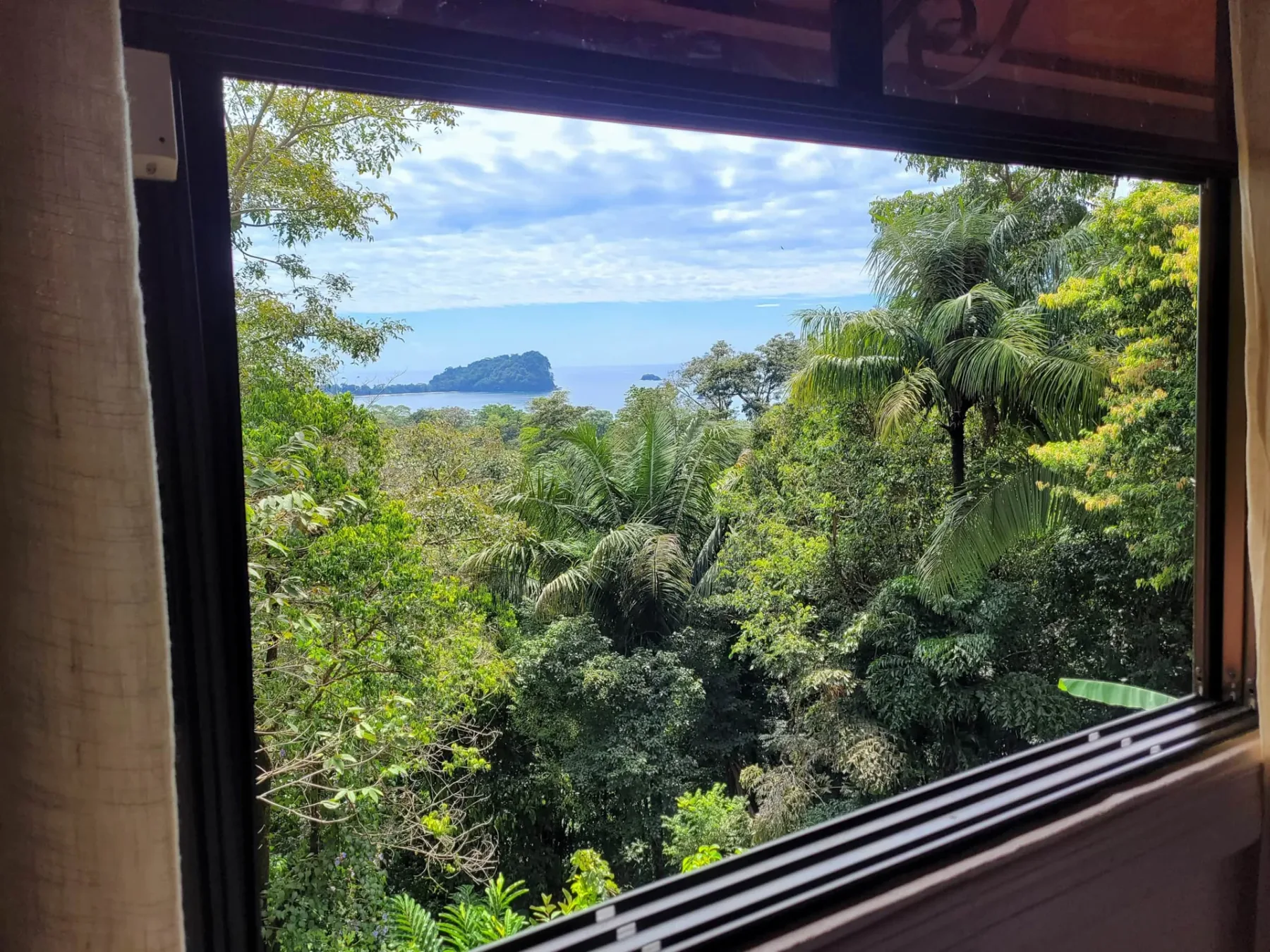 A large window overlooks dense tropical greenery, blue ocean, and a distant island.