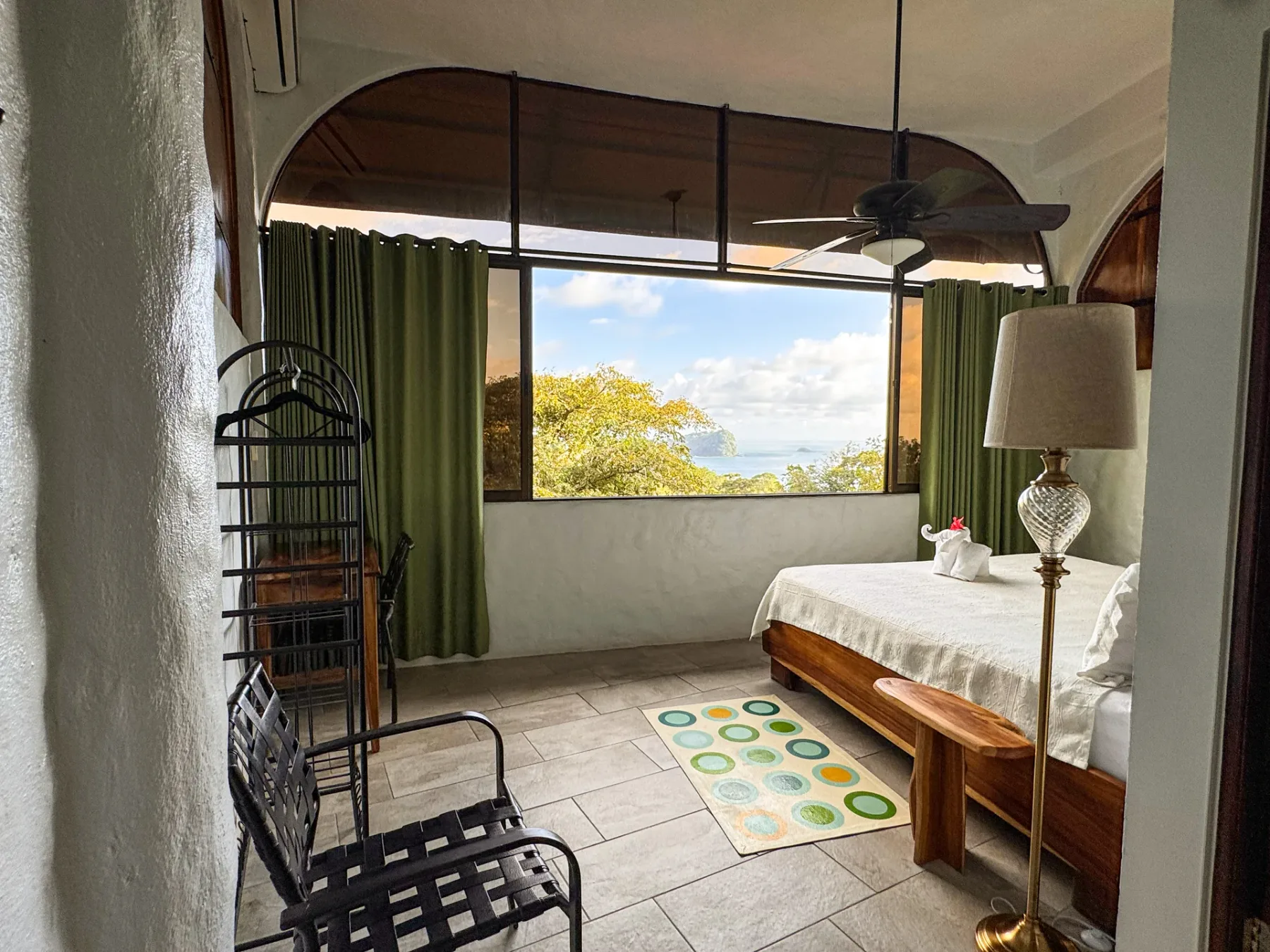 A bedroom with a bed beside a large window overlooking trees and water.