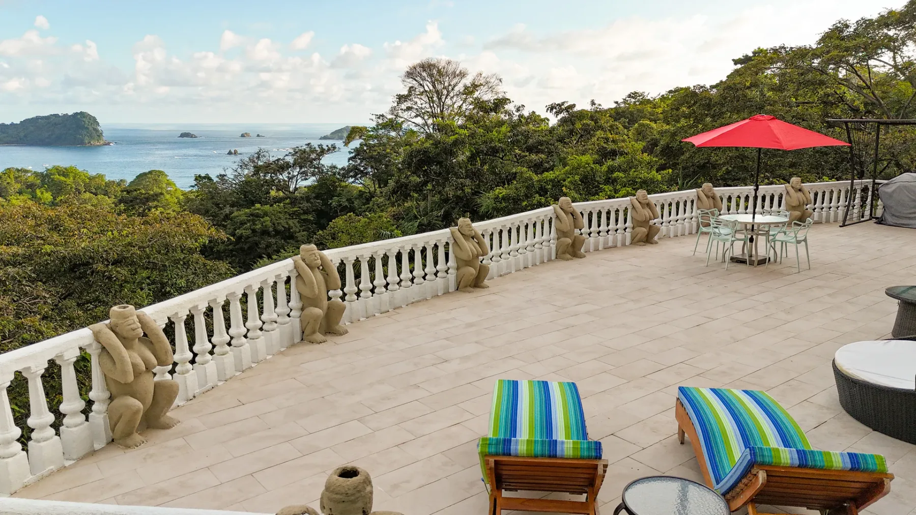 A spacious tiled terrace overlooks a tree-lined coastline and the sea.
