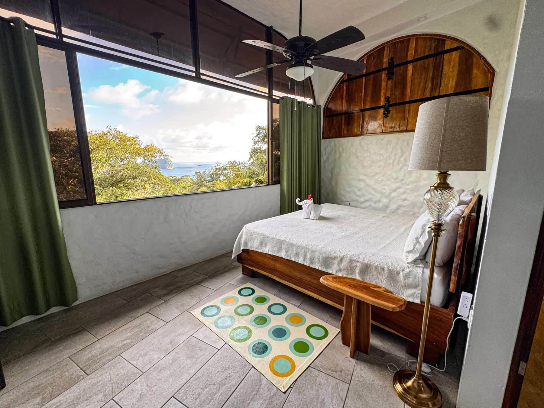 A bedroom with a bed beside a large window overlooking trees and water.