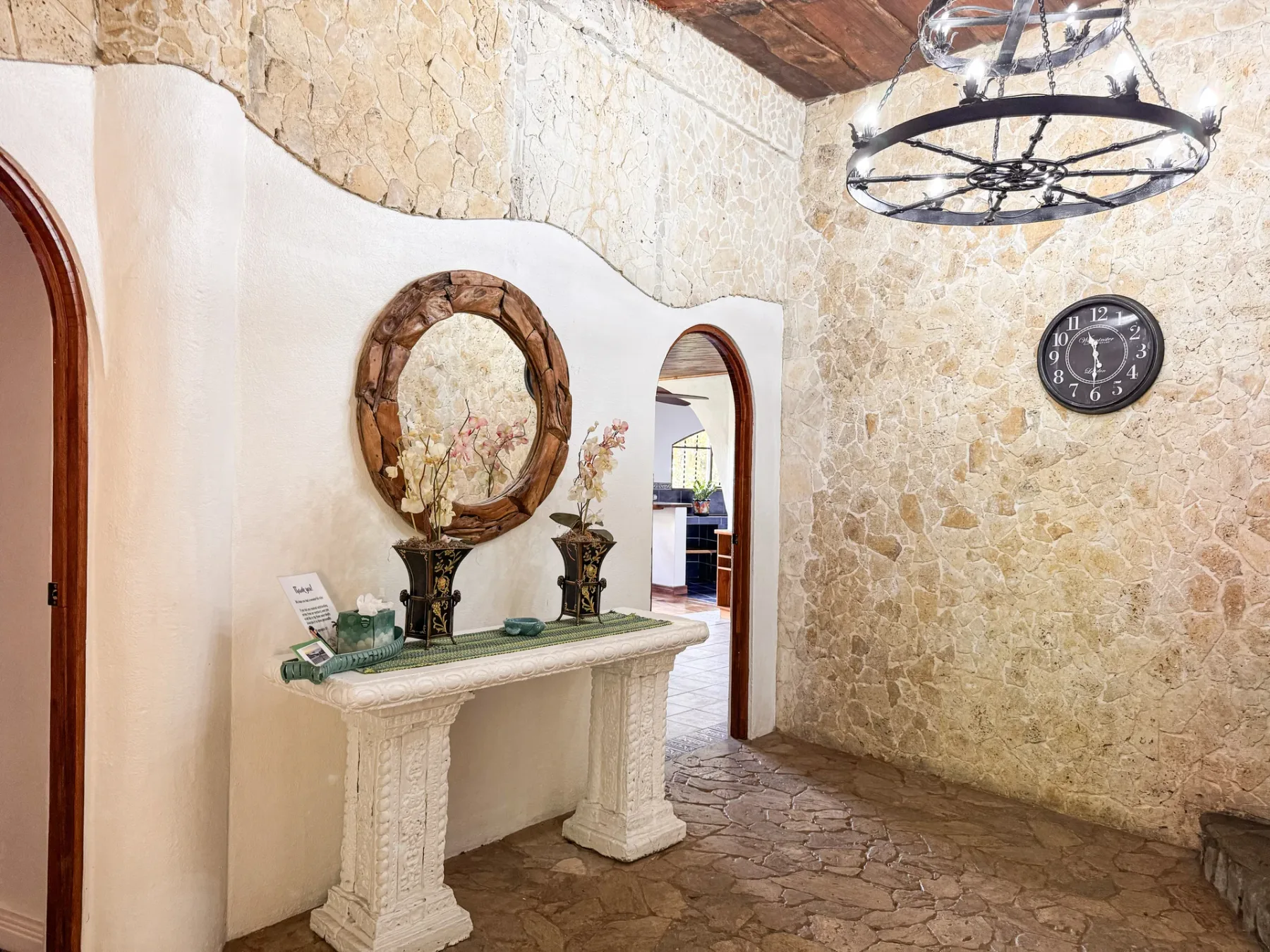 A stone hallway features an ornate console table and arched openings.