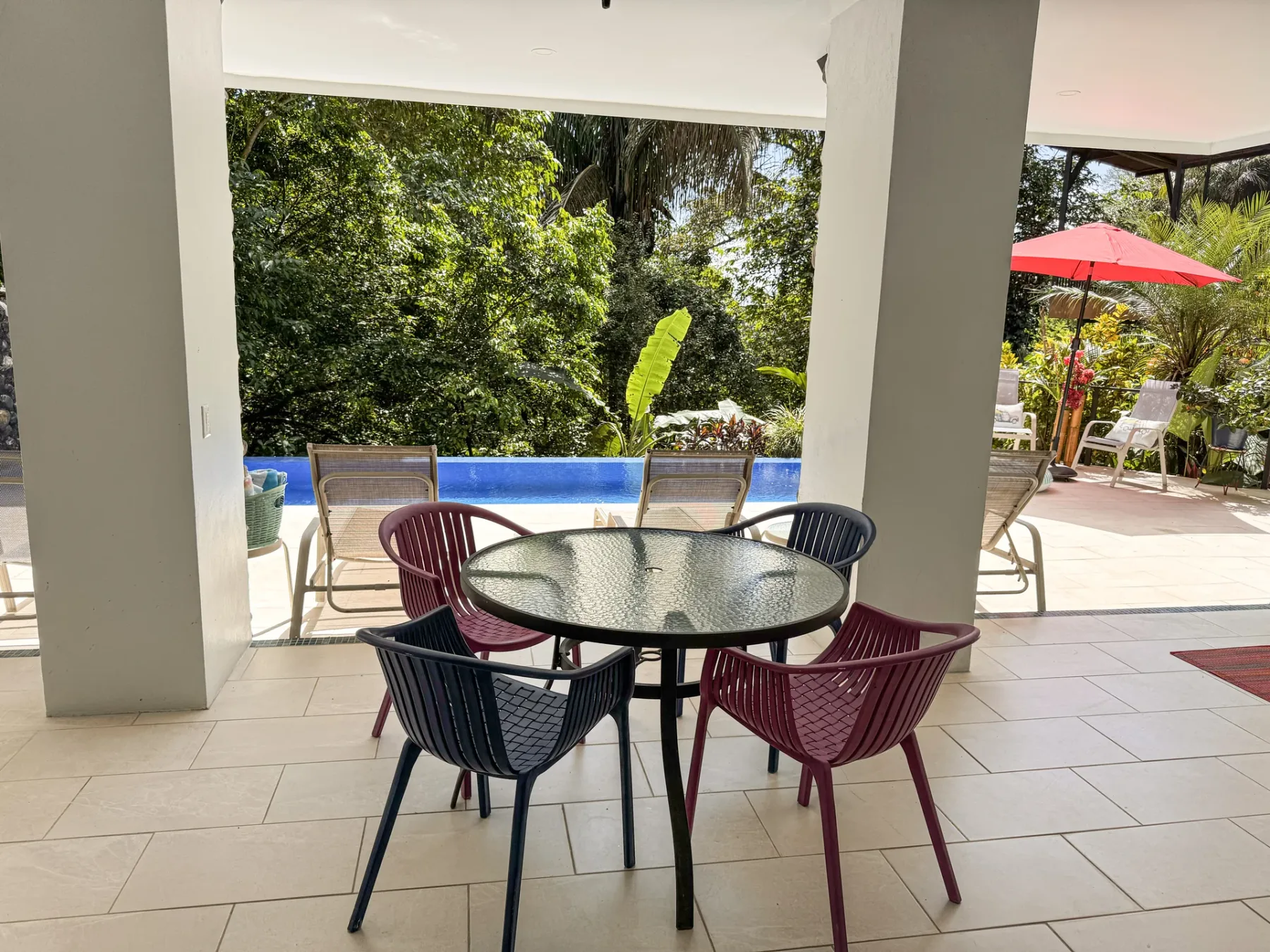 A covered patio seating area overlooks a swimming pool and leafy garden.