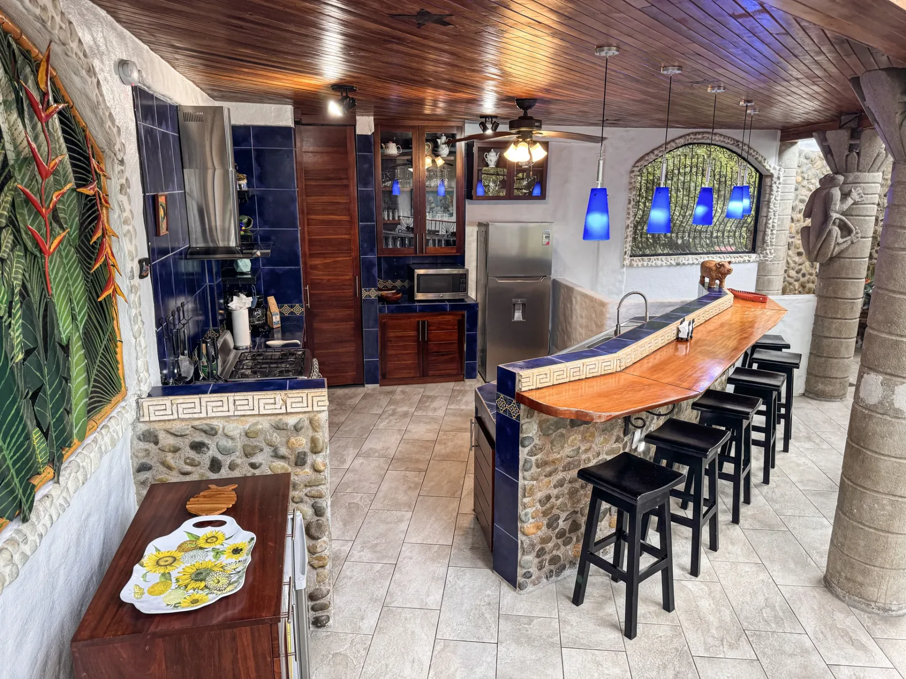 A kitchen and bar area with a long counter, stools, and blue pendant lights.