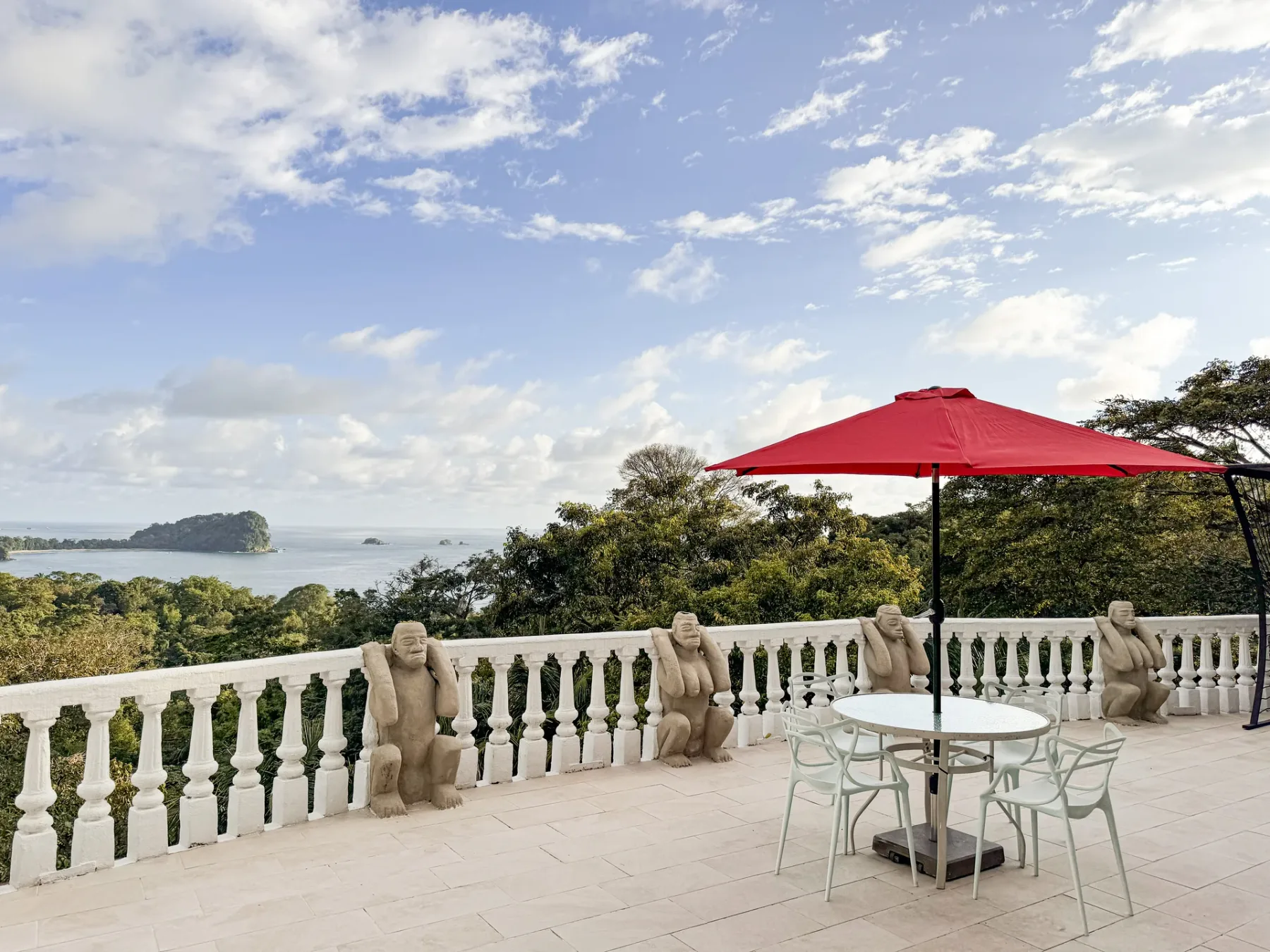 An outdoor terrace with a dining table and red umbrella overlooks the water.