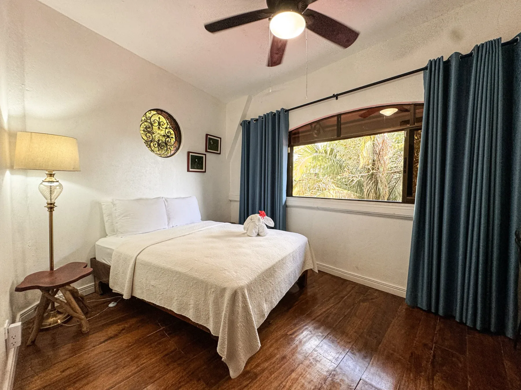 A bedroom with a neatly made bed, blue curtains, and a large window.