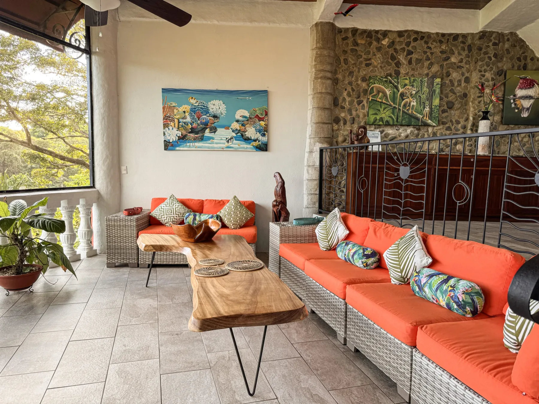 A bright living room has woven seating with orange cushions and wooden coffee tables.
