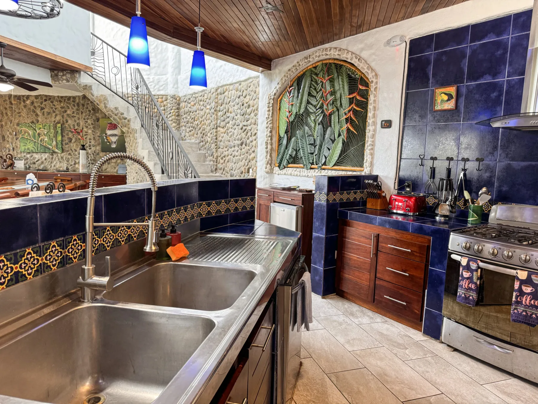 A kitchen with a large sink, tiled counters, and a stove.