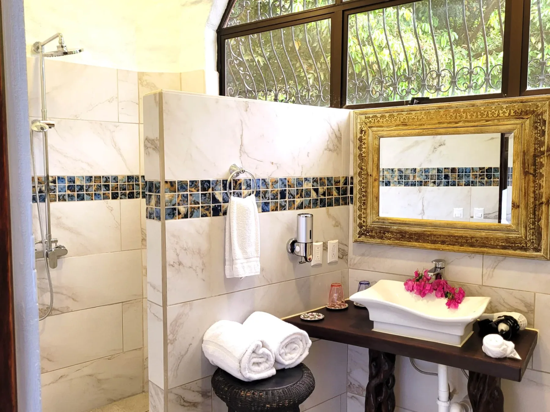 A bathroom with a glass shower, a sink, and a gold-framed mirror.