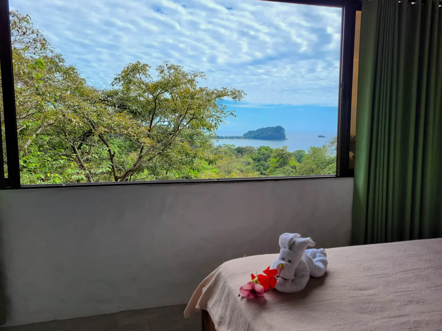 A bedroom with a wide window overlooking trees, water, and a small island.