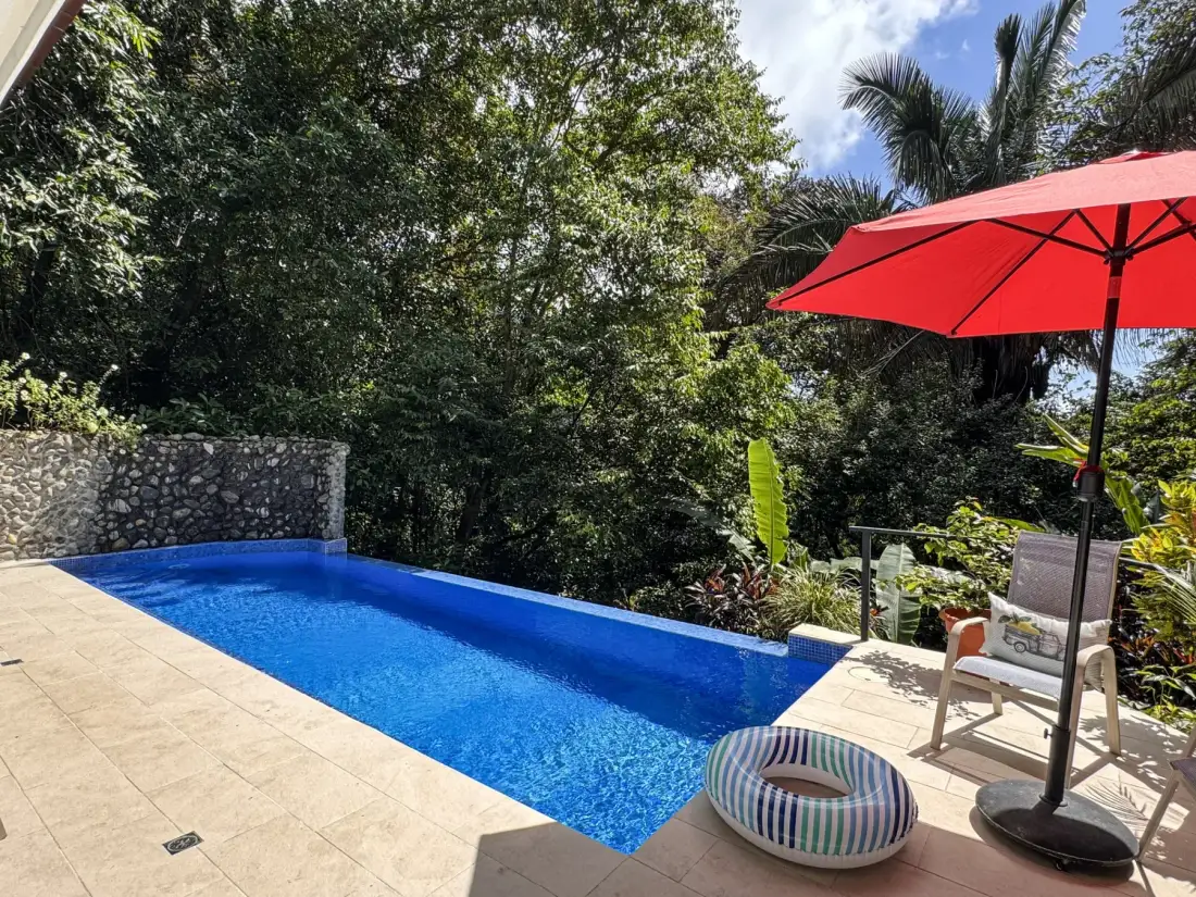 An outdoor swimming pool sits beside a tiled patio and red umbrella.