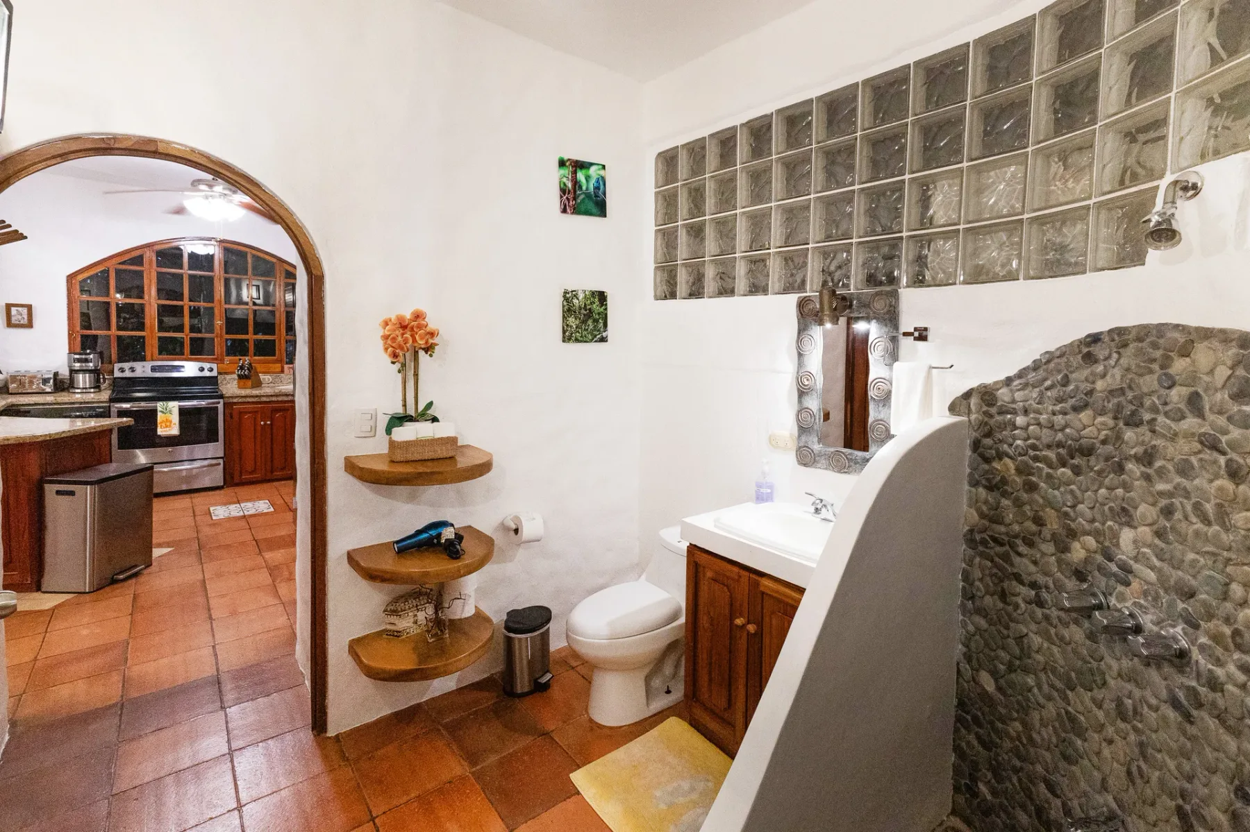 A bathroom with a sink and toilet beside an arched opening to the kitchen.