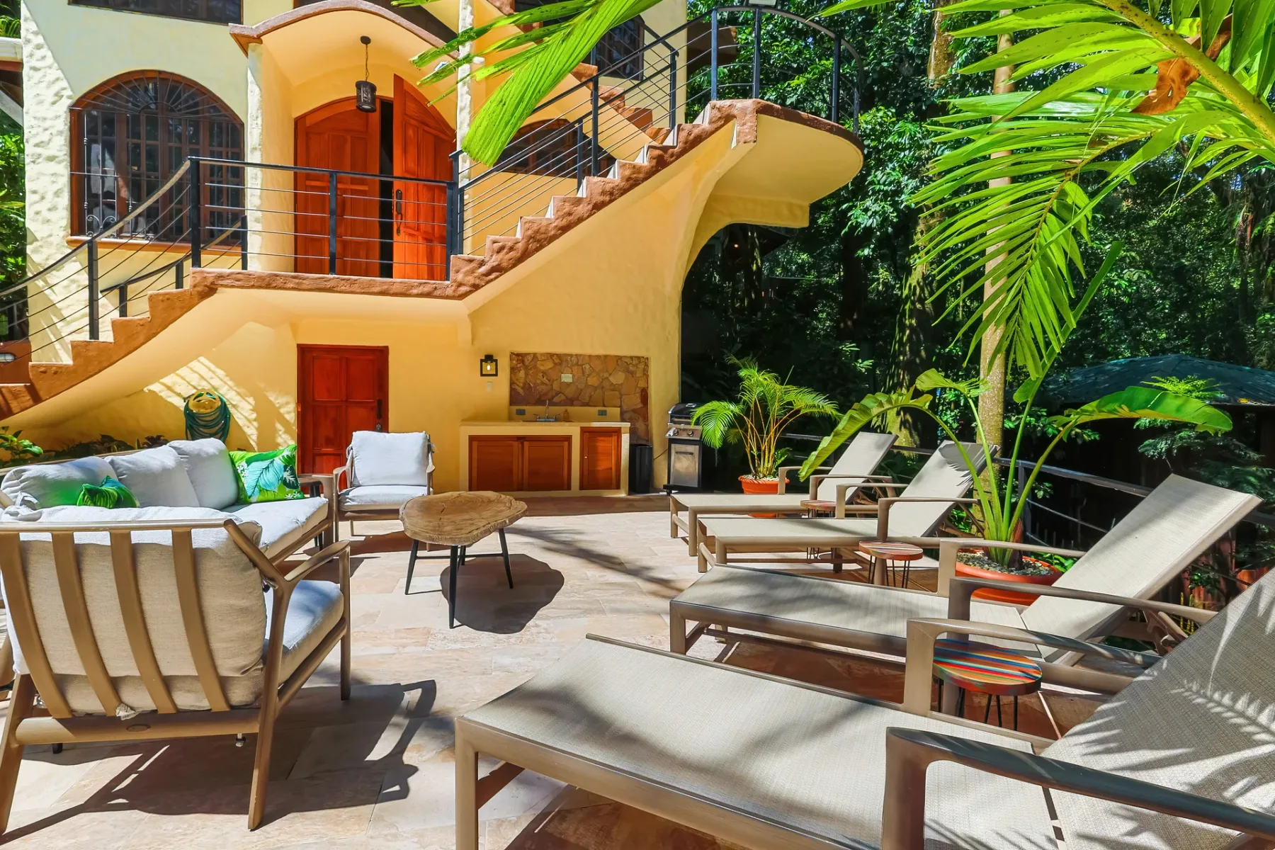 An outdoor patio with seating, a table, and a staircase beside the house.