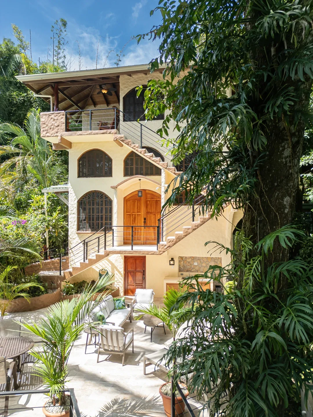 A multi-level house with exterior stairs overlooks a patio with outdoor seating.