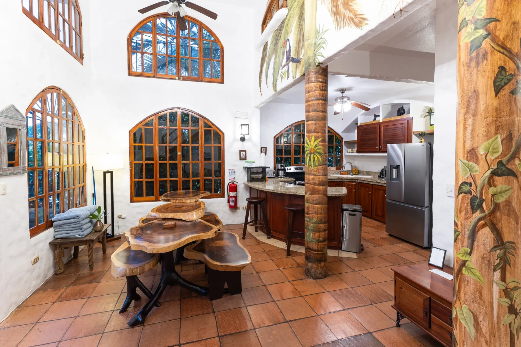 An open kitchen and dining area with wooden tables, tiled flooring, and a refrigerator.