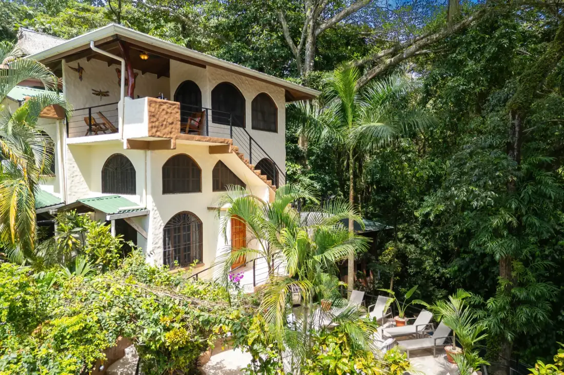 A multi-level house with arched windows sits among dense tropical greenery.
