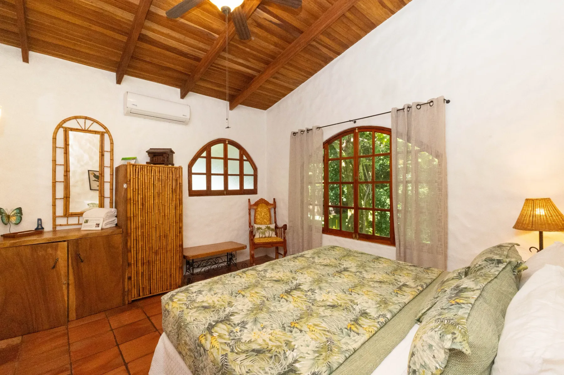 A bedroom with a bed, wooden furnishings, and a large curtained window.