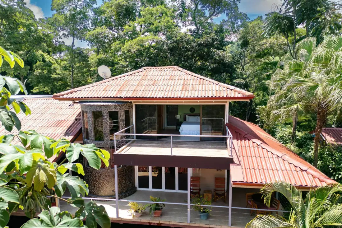 Una casa con techo de tejas y balcones está rodeada de abundante vegetación.