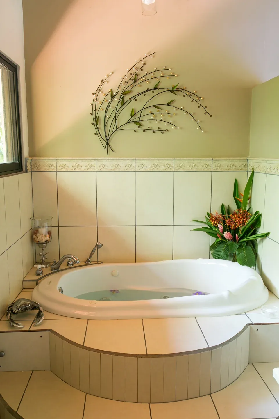 Un baño cuenta con una bañera empotrada, paredes de azulejos y plantas decorativas.