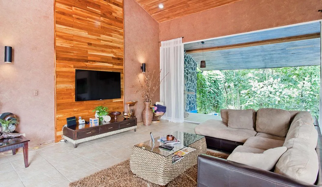 Una sala de estar con asientos alrededor de una mesa de centro, frente a un televisor en la pared.