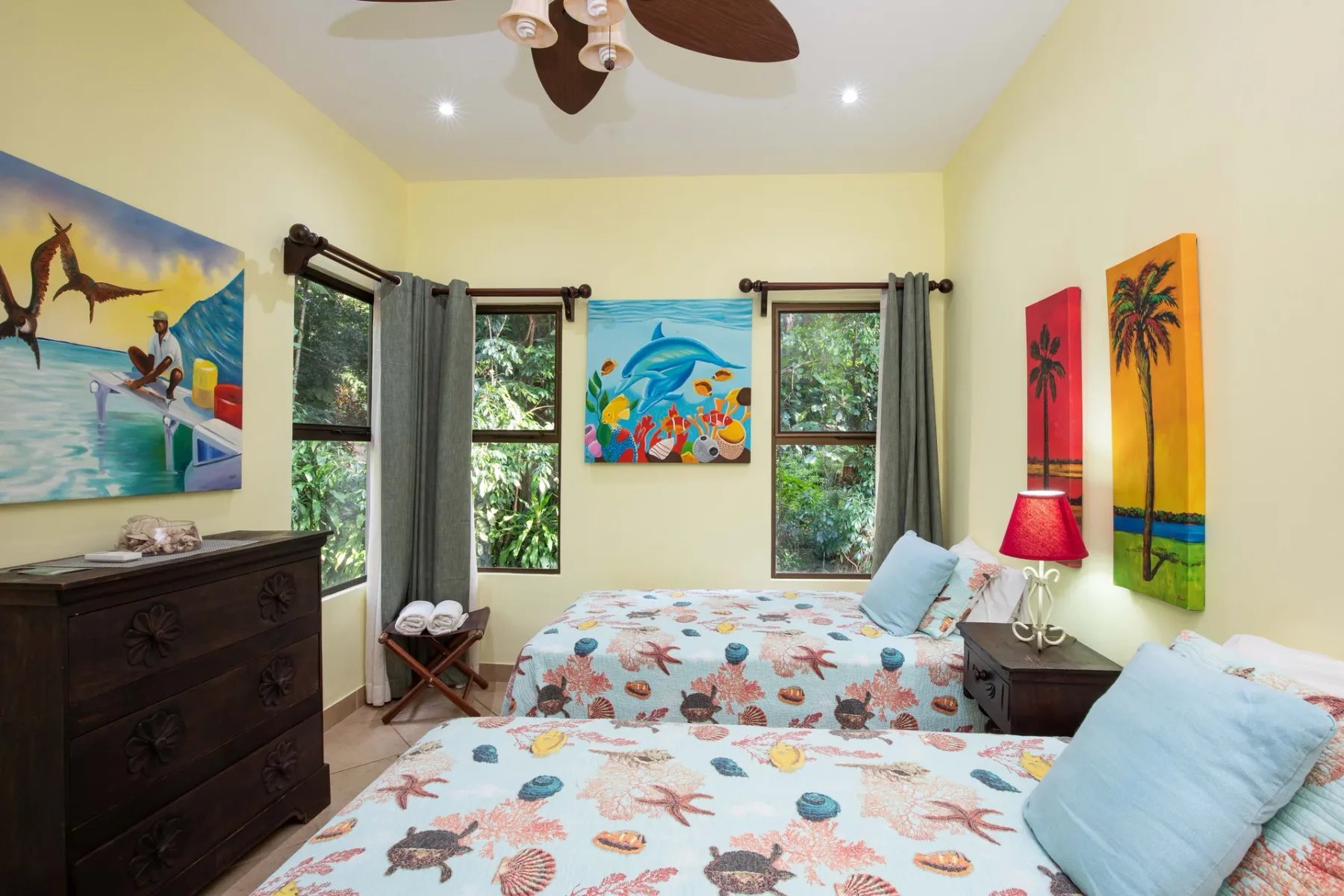 A bedroom with two beds, colorful sea-life bedding, and tropical wall art.