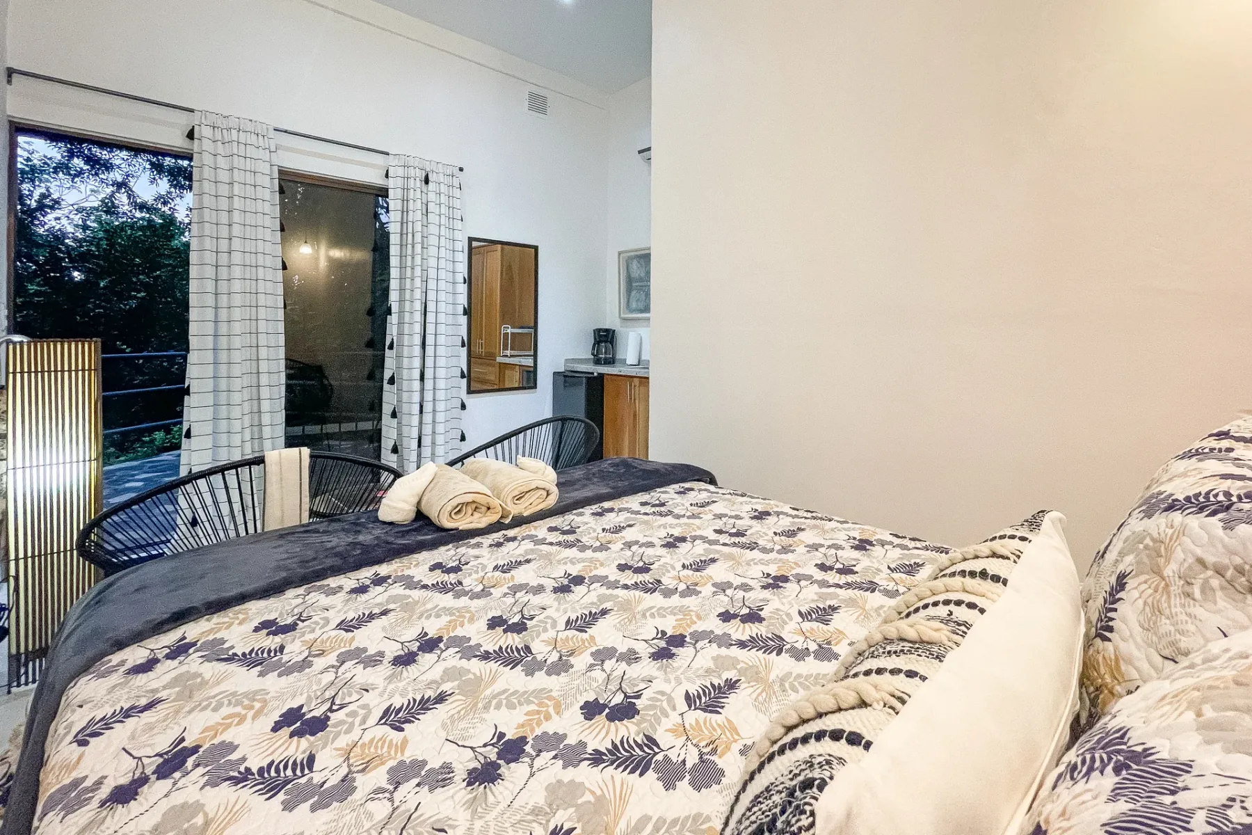 A bedroom with a patterned bedspread and windows overlooking greenery.